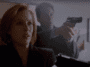 Dana Scully (Gillian Anderson), a woman with short red hair wearing a dark blazer, holds up a pistol. Fox Mulder (David Duchovny) stands behind her; he wears a suit and also has a pistol raised.