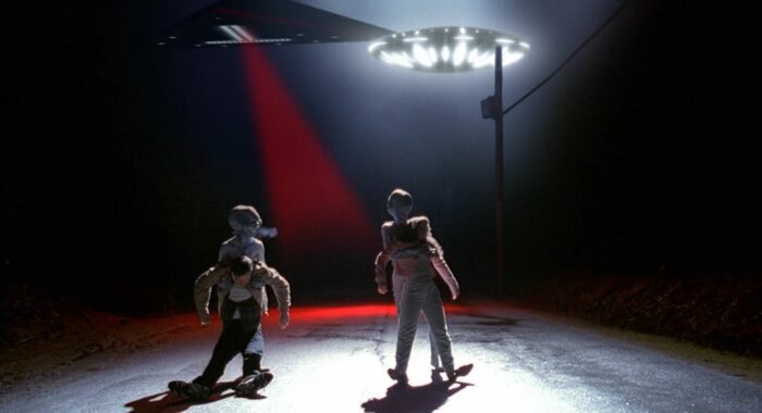 Two aliens dragging bodies towards a flying saucer