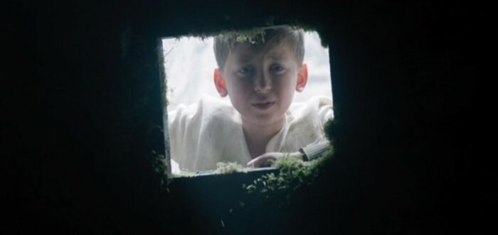 Josiah peers down through a square hole into a dark space