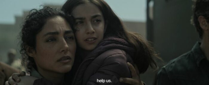 Aneesha holds Sarah while a subtitle reads "help us"