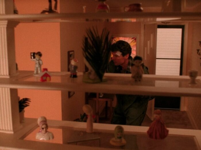 Ed enters his house, with a shelf of figurines in the foreground, one of which has an eye patch, in Twin Peaks Episode 2