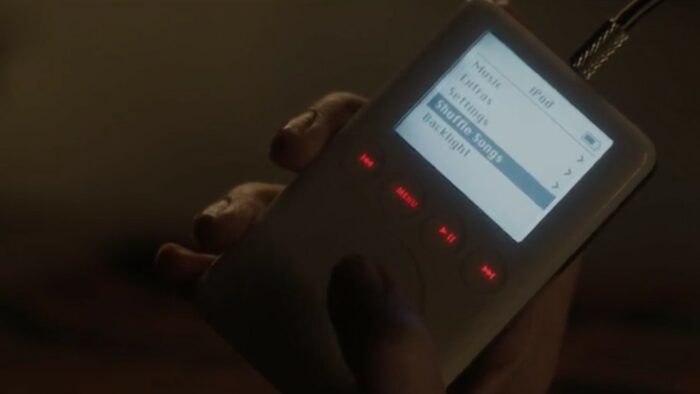 A Murder at the End of the World S1E2 - An iPod is held in someone's hand, Shuffle Songs mode is selected