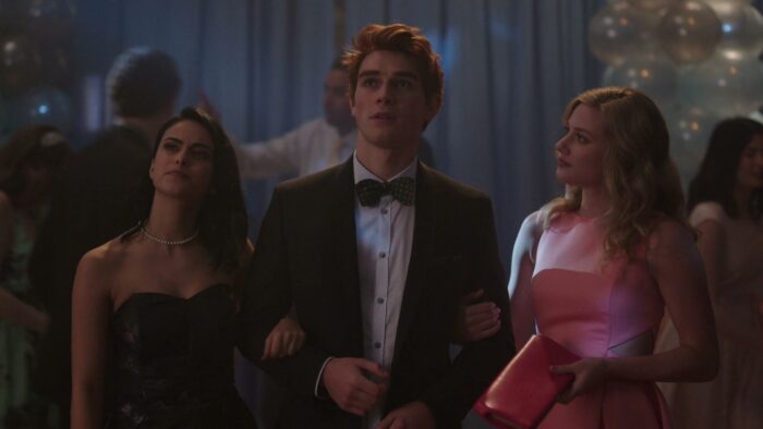 A young man stands with two young women at a school dance
