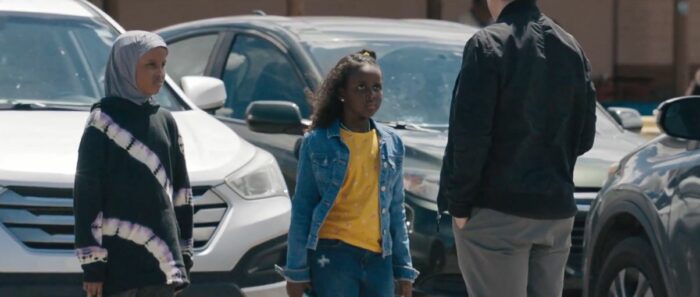 A young Somali girl in a jean jacket and yellow shirt stands in a parking lot in The Curse on Showtime