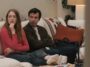 Whitney and Asher sit on a couch with their heads turned towards a TV in The Curse S1E3, "Questa Lane"