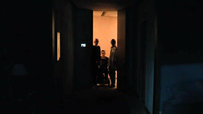 A Murder at the End of the World S01E06 - Lee, Oliver, and Darby are silhouetted in the doorway of a dark room, doorbell cam screen just to the left