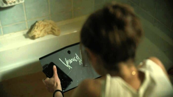 A Murder at the End of the World S01E06 - Darby kneels at the bathtub, holding Bill's laptop in her hands, "FANGS" written on the bottom facing her