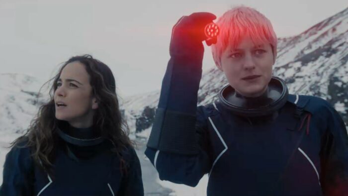 Darby and Sian stand on the snowy bluff, Darby using the red signalling light