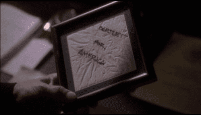 A closeup of Leo's hands, holding the framed cocktail napkin that says "Bartlet For America"