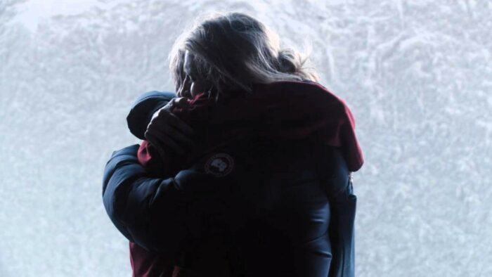 Lee and Darby hug tightly standing in front of a wall of snow