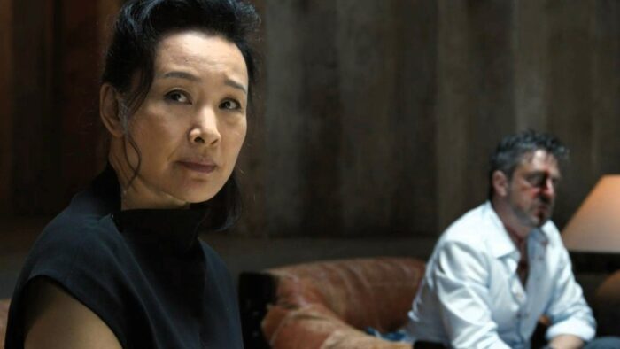 A Murder at the End of the World S01E07 - Lu Mei sits looking distraught, a beaten up David sits in another chair behind her
