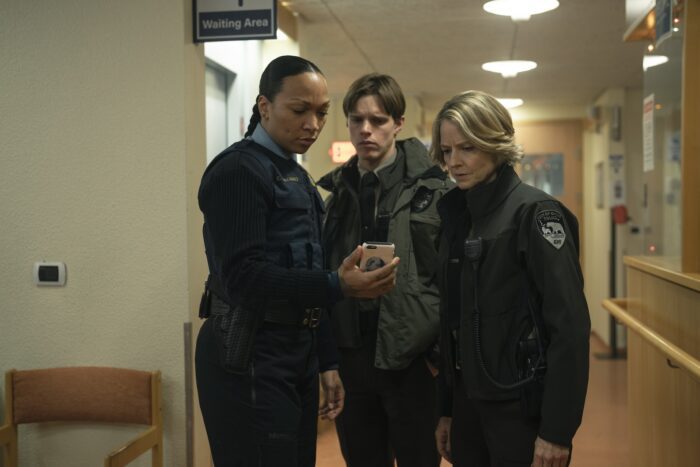 Navarro, Pete and Danvers huddle in a hospital hall looking at a phone in True Detective: Night Country Part 3