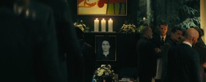 A picture of Jo with three candles above it and flowers below, with people milling around