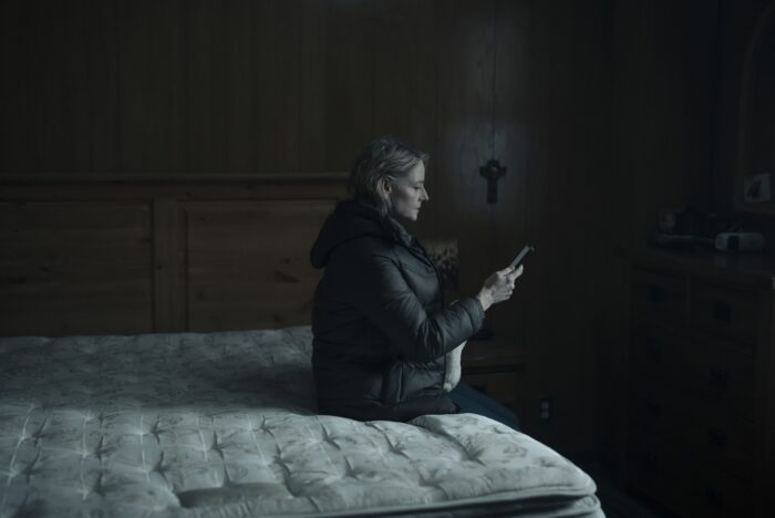 Danvers sits on a bed looking at a phone
