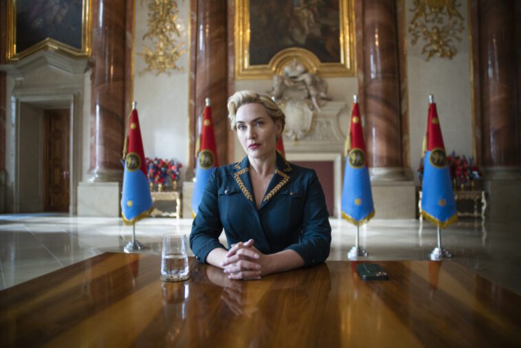Kate Winslet sits at a table in The Regime on HBO