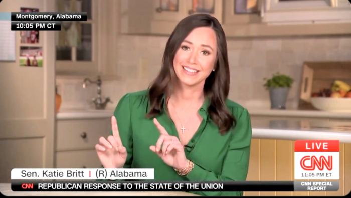 Katie Britt points her fingers upwards in a kitchen