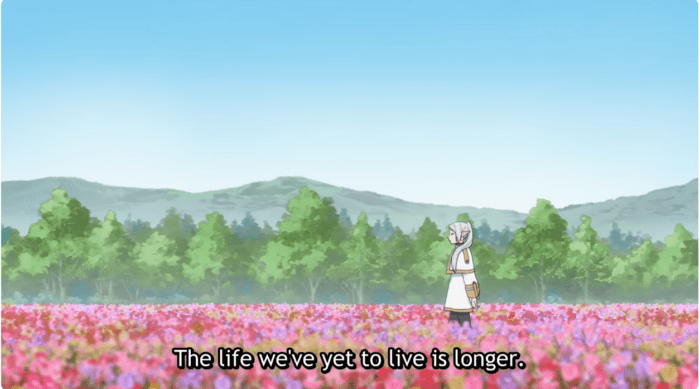 A wide shot of a colorful landscape. Frieren, an elf with long grey hair and a white robe, walks through a dense field of colorful flowers. Below her, the caption reads, "The life we've yet to live is longer."
