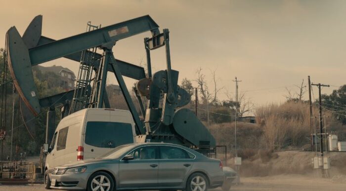 A car pulling up behind Charlie's van, which is parked in front of an oil rig